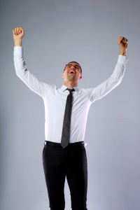 Happy businessman standing with hands raised up over gray background